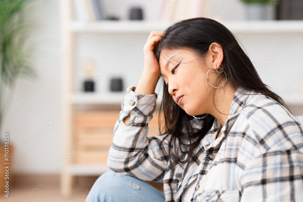 Sad and pensive woman sitting at home leaning her head on hand Sad and pensive woman sitting at home leaning her head on hand
