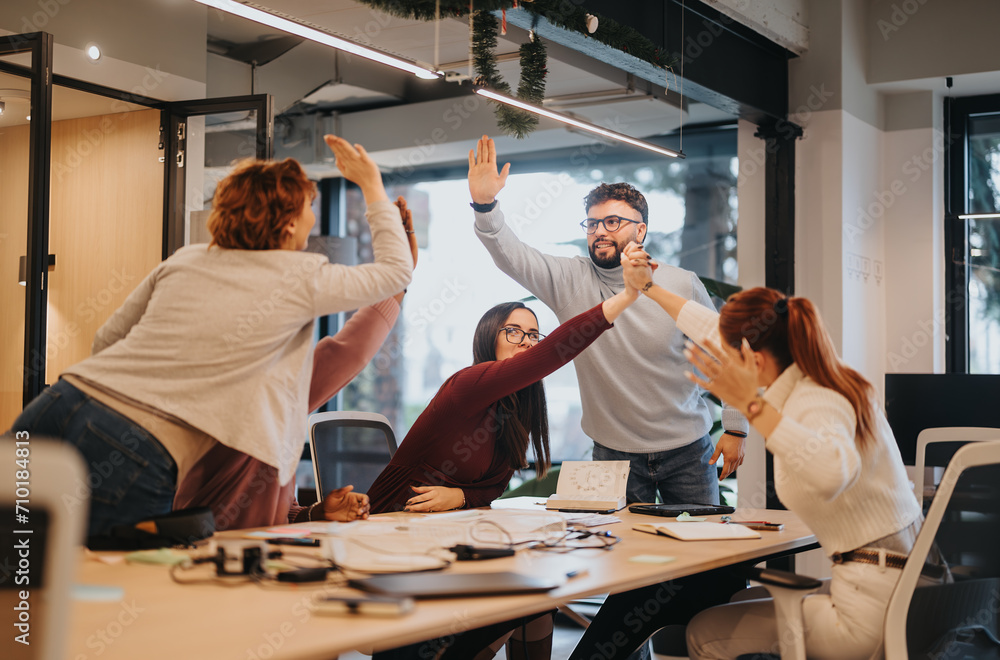 Obraz premium Multicultural colleagues celebrating a successful project in the office. Business people caught up in a moment of victory, smiling and overjoyed with positive outcomes.