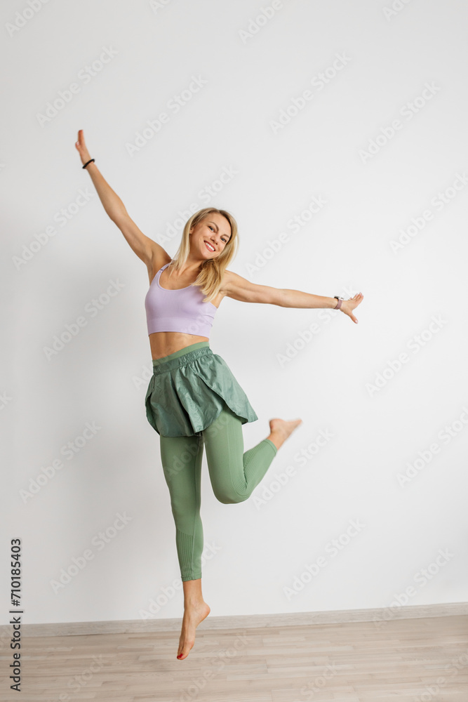 Happy athletic woman dancing in modern fitness attire, white background.