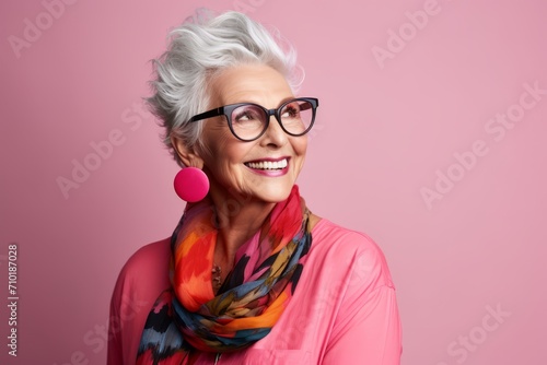 Cheerful senior woman in eyeglasses and scarf posing on pink background