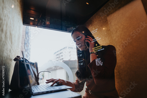 A businesswoman in a phone booth discussing a project and negotiating with a client. Busy office environment with employees working and having meetings. Dedicated to company growth and profit. photo