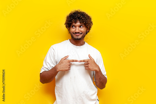 modest young indian man in white t-shirt feeling shy and worried on yellow isolated background, introvert guy feeling uneasy