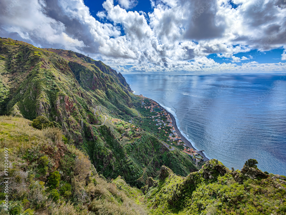 Scenic view over Paul do Mar village at the west coast of Madeira Island. Green mountains, roads, blue ocean and sky with white clouds landscape
