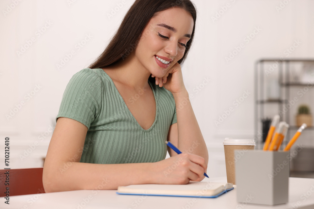 Young woman writing in notebook at white table indoors Young woman writing in notebook at white table indoors