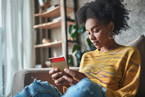 Young adult African American female consumer holding credit card and sitting on floor at home doing online banking transaction. E commerce virtual shopping, secure mobile banking, Generative AI photo
