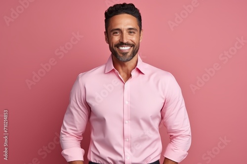 Handsome young man in pink shirt looking at camera and smiling while standing against pink background