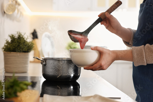 Woman pouring tasty soup into bowl at countertop in kitchen, closeup photo