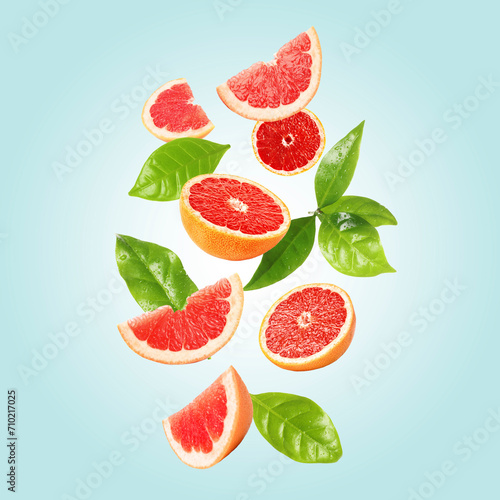 Fresh grapefruit pieces and green leaves falling on light blue background