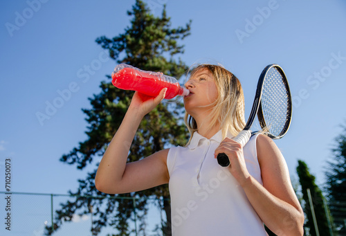 Female athlete on tennis court drinking energy drink  photo