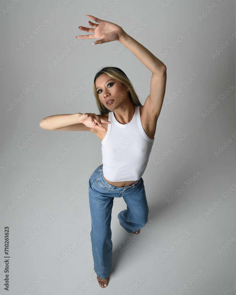Full length portrait of brunette female asian model wearing casual clothes, white singlet shirt, denim jean pants. Standing pose, high camera angle for perspective. Isolated on white studio background Full length portrait of brunette female asian model wearing casual clothes, white singlet shirt, denim jean pants. Standing pose, high camera angle for perspective. Isolated on white studio background