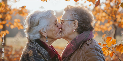 Senior gay lesbian couple in love kissing outside while walking in autumn park. LGBTQ aged tourists having tender moment during spring vacation. Romantic scene between two loving women