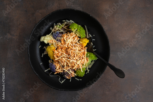 Bowl of cooked rainbow cauliflower topped with shredded chicken and grated parmesan cheese with a fork, part of a nutritious meal
