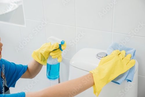 Diligent woman in rubber gloves scrubs toilet seat with cloth ensuring purity in bathroom cleaning. Her dedication a maid showcases meticulous housekeeping and hygiene. Housekeeper healthcare concept