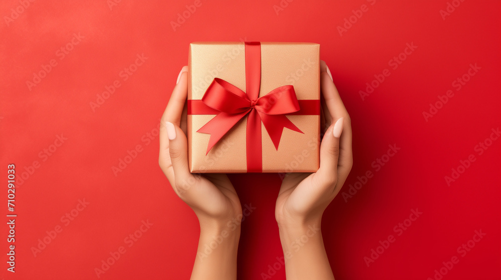 Top down view of a woman hands holding a luxury gift box with bow against a red background Top down view of a woman hands holding a luxury gift box with bow against a red background