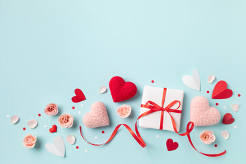 Valentine day or mother day festive composition with gift or present box, rose flowers and red pink hearts on pastel blue background from above. Flat lay style..