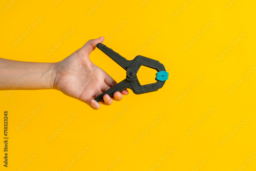 Black plastic spring clamp in hand isolated on yellow background Black plastic spring clamp in hand isolated on yellow background