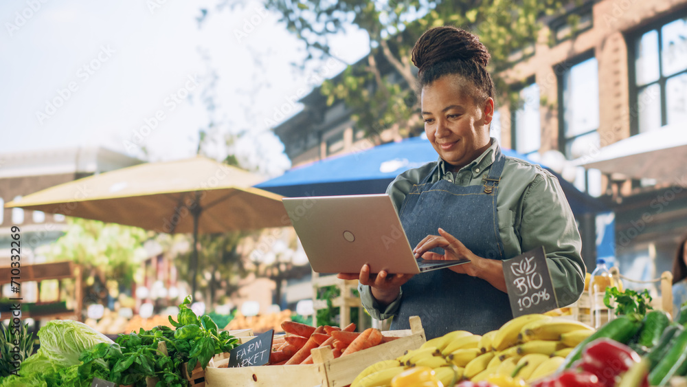 Portrait of a Black Female Running a Street Vendor Food Stand with Fresh Organic Agricultural Products. Farmer Using Laptop Computer to Manage Business Operations, Online Orders and Marketing Campaign - obrazy, fototapety, plakaty 