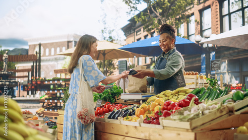 Beautiful Female Customer Buying Sustainable Organic Vegetables From a Joyful Black Female Farmer on a Sunny Summer Day. Successful Street Vendor Managing a Farm Stall at an Outdoors Eco Market photo