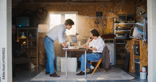 Two Caucasian Male Stock Traders Working In Retro Garage, Using Old Computer With Candlestick Chart And Landline Phone To Pitch A Public Company To Investors. Partners Celebrating Successful Sale. photo