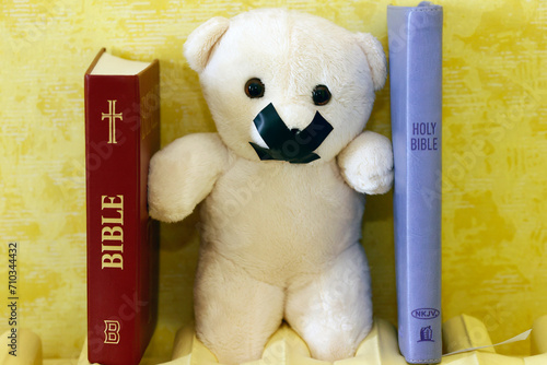 Bibles and teddy bear with tape on his mouth. Symbol of silence on child abuse and victim in christian church.