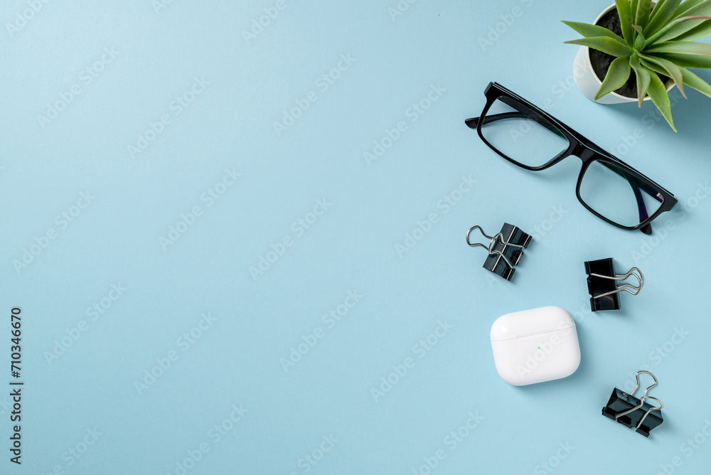 Top view of Glasses, black binder paper clip and headphones on blue table Top view of Glasses, black binder paper clip and headphones on blue table