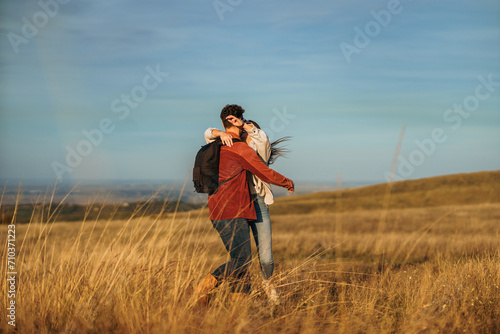 A happy couple is hugging and having a great time on a big golden yellow meadow on a sunny autumn day.