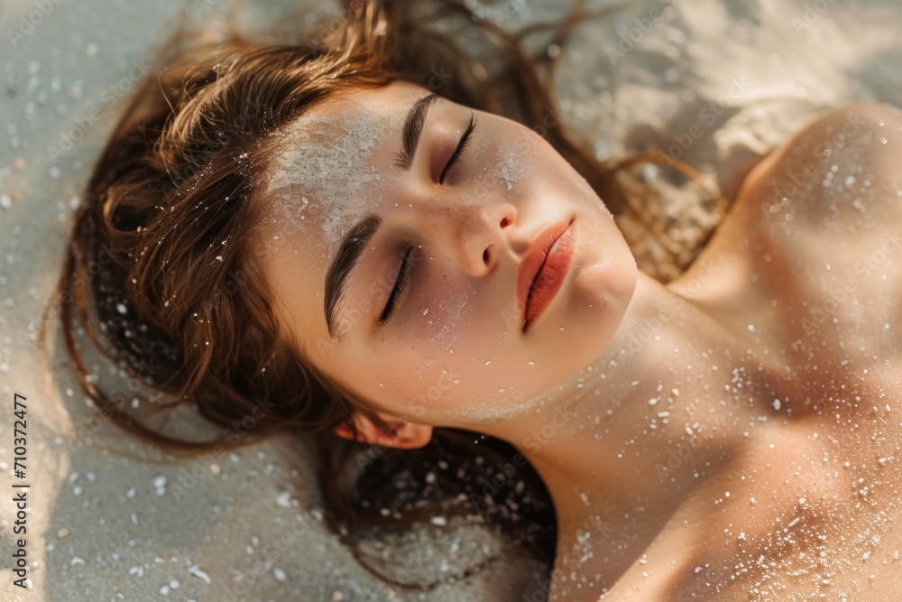 Portrait of a young woman lying in the sand on a beach, her face covered with grains of sand.