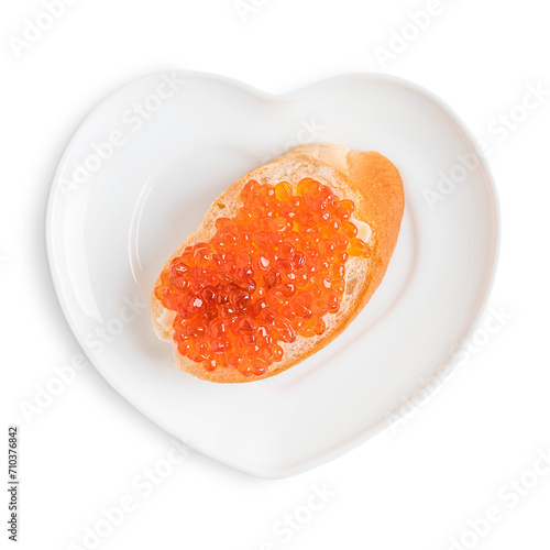 Top view of sliced bread with butter and red salted salmon fish caviar served on heart shaped plate isolated on white background prepared for healthy breakfast full of protein, omega 3 and vitamins