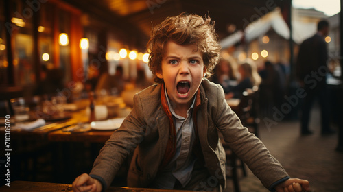 Toddler having a temper tantrum in a restaurant or cafe. Sad child screaming in anger in public. photo