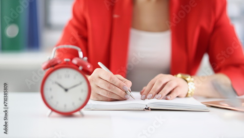 Businesswoman makes notes in documents there is an alarm clock next to it. Time tracking and employee deadlines concept photo