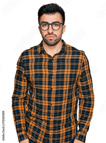 Hispanic man with beard wearing casual clothes and glasses with serious expression on face. simple and natural looking at the camera.