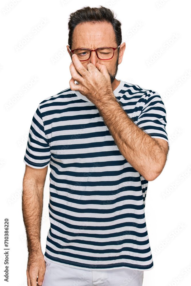 Middle age man wearing casual clothes and glasses smelling something stinky and disgusting, intolerable smell, holding breath with fingers on nose. bad smell Middle age man wearing casual clothes and glasses smelling something stinky and disgusting, intolerable smell, holding breath with fingers on nose. bad smell