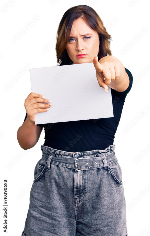 Young beautiful caucasian woman holding blank empty paper pointing with finger to the camera and to you, confident gesture looking serious