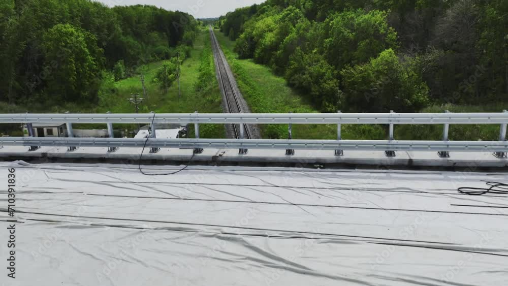 Railroad tracks under road bridge under construction among forest. Railway line running through thick forest beneath cloth covered bridge Railroad tracks under road bridge under construction among forest. Railway line running through thick forest beneath cloth covered bridge