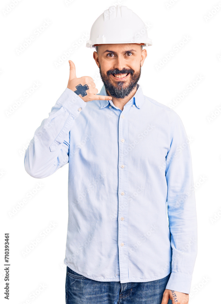 Young handsome man wearing architect hardhat smiling doing phone gesture with hand and fingers like talking on the telephone. communicating concepts. Young handsome man wearing architect hardhat smiling doing phone gesture with hand and fingers like talking on the telephone. communicating concepts.