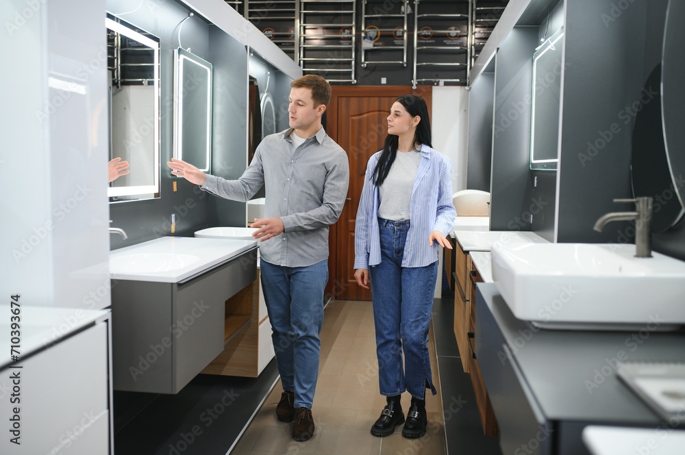 Young couple choosing new bathroom furniture at the plumbing shop with lots of sanitary goods