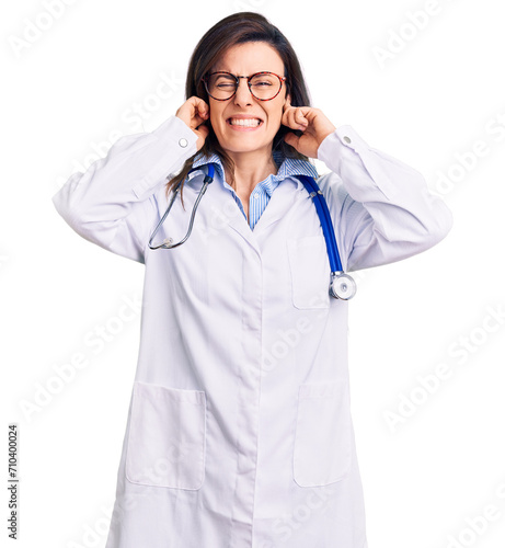Young beautiful woman wearing doctor stethoscope and glasses covering ears with fingers with annoyed expression for the noise of loud music. deaf concept.