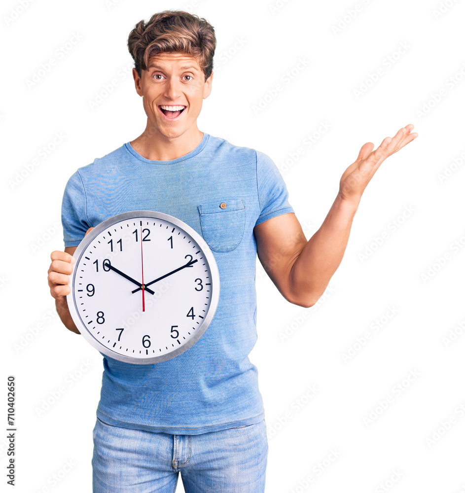 Young handsome man holding big clock celebrating victory with happy smile and winner expression with raised hands Young handsome man holding big clock celebrating victory with happy smile and winner expression with raised hands