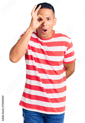 Young handsome latin man wearing casual clothes doing ok gesture shocked with surprised face, eye looking through fingers. unbelieving expression.