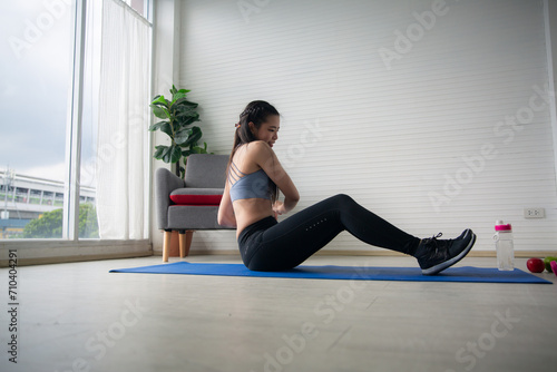 A Sporty young woman enjoy doing morning exercise alone in living room, beautiful Asian female wearing sportswear doing weight training or practicing muscles workout at home for healthy body wellness.
