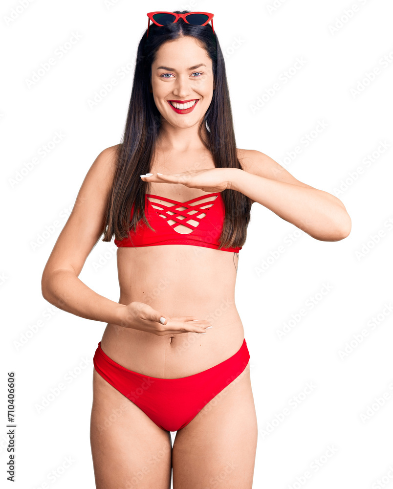Young beautiful caucasian woman wearing bikini gesturing with hands showing big and large size sign, measure symbol. smiling looking at the camera. measuring concept. Young beautiful caucasian woman wearing bikini gesturing with hands showing big and large size sign, measure symbol. smiling looking at the camera. measuring concept.