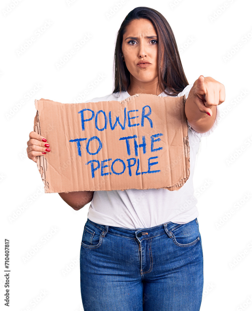 Young beautiful woman holding power to the people cardboard banner pointing with finger to the camera and to you, confident gesture looking serious Young beautiful woman holding power to the people cardboard banner pointing with finger to the camera and to you, confident gesture looking serious