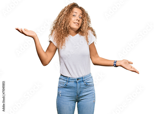 Beautiful caucasian teenager girl wearing casual white tshirt clueless and confused expression with arms and hands raised. doubt concept.