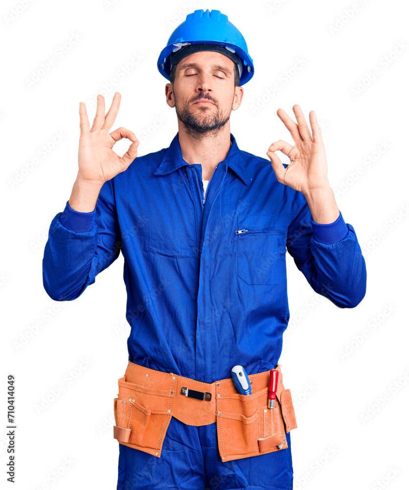 Young handsome man wearing worker uniform and hardhat relaxed and smiling with eyes closed doing meditation gesture with fingers. yoga concept. Young handsome man wearing worker uniform and hardhat relaxed and smiling with eyes closed doing meditation gesture with fingers. yoga concept.