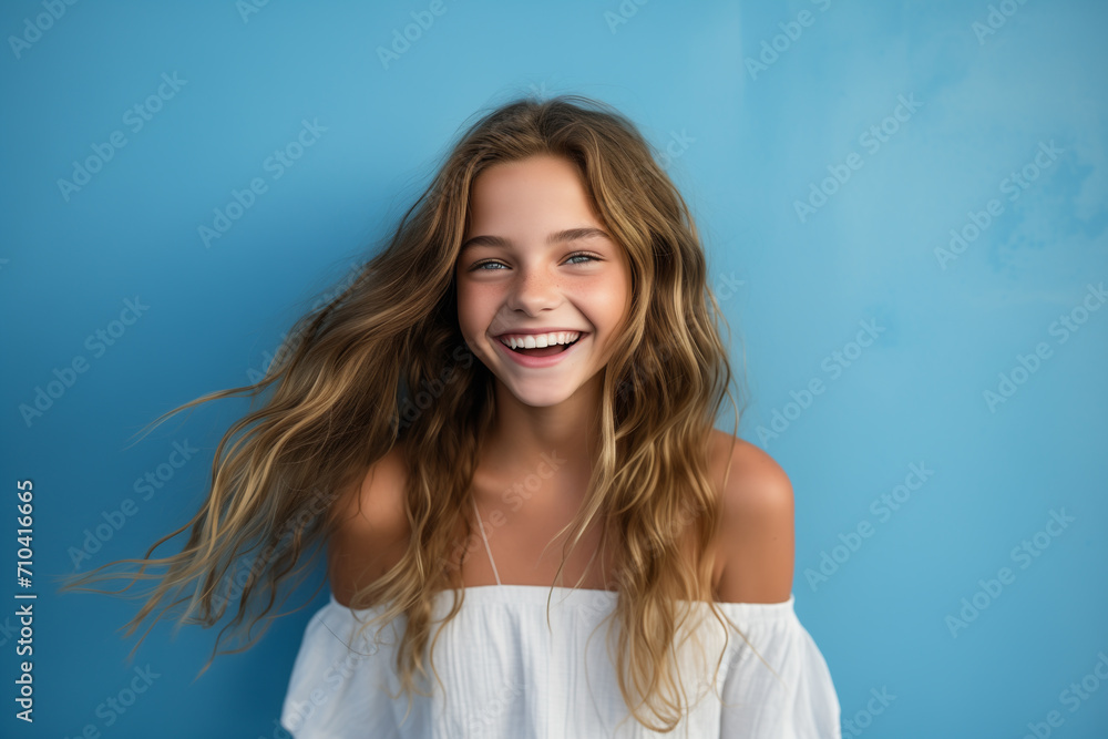Waist up shot of happy curly girl with toothy smile, wears white shirt, expresses good emotions, enjoys nice day, isolated over blue background. Face expressions Waist up shot of happy curly girl with toothy smile, wears white shirt, expresses good emotions, enjoys nice day, isolated over blue background. Face expressions