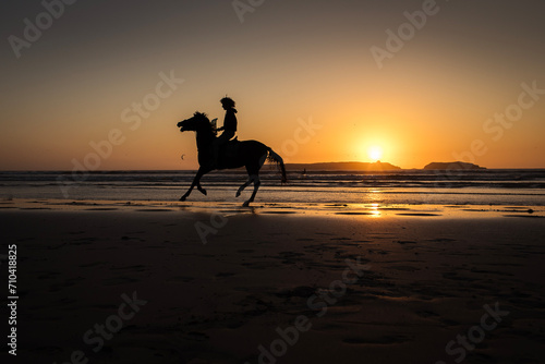 Silhouette of horse riding on the beach with reflection at sunset in background. Essaouira, Morocco