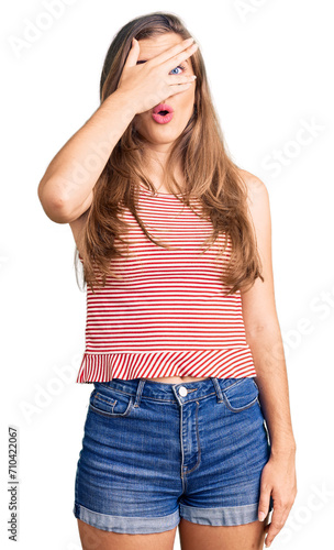 Beautiful caucasian young woman wearing casual clothes peeking in shock covering face and eyes with hand, looking through fingers with embarrassed expression.