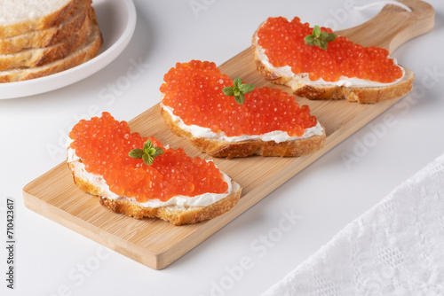 Three sandwiches with red caviar on a cutting board. A delicious appetizer of trout caviar on a slice of bread with cream cheese. Salted salmon caviar for fish delicacy concept