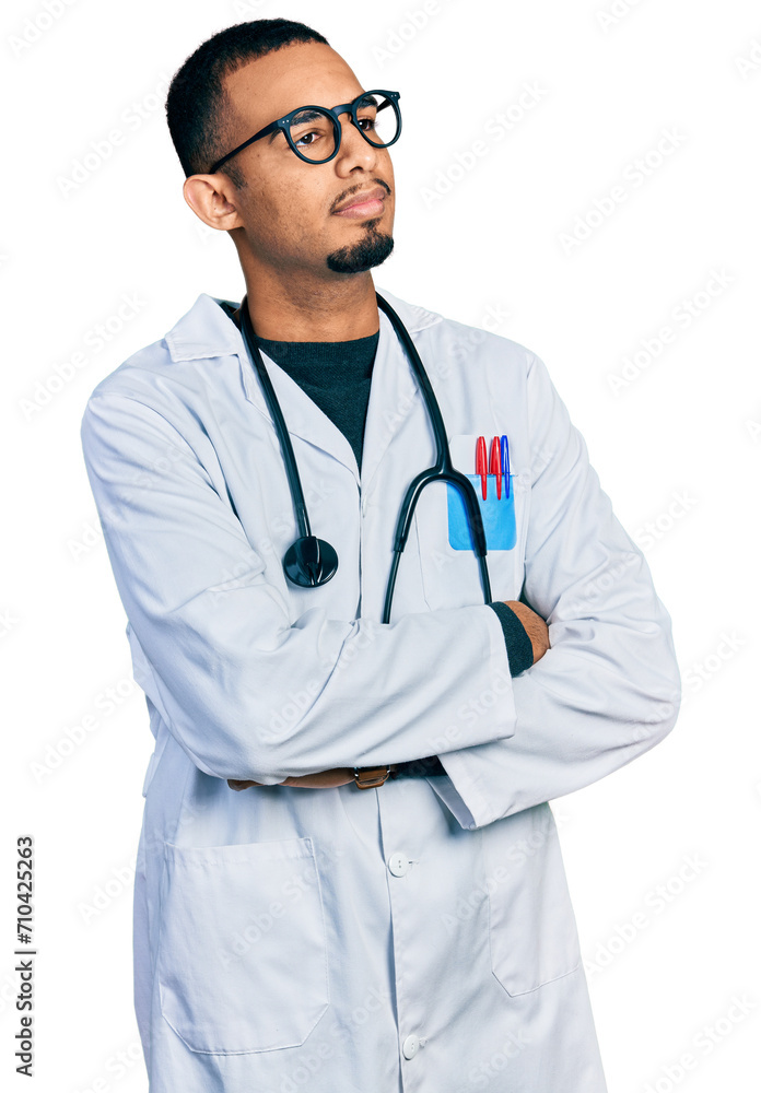 Young african american man wearing doctor uniform and stethoscope looking to the side with arms crossed convinced and confident Young african american man wearing doctor uniform and stethoscope looking to the side with arms crossed convinced and confident