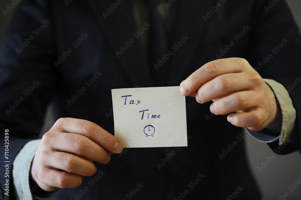 Businessman in a suit hand holding sticker with tax time Businessman in a suit hand holding sticker with tax time